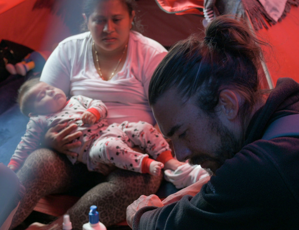Christopher Rios, Stanford Global Health Media Fellow, interviews Honduras migrant, Mildre, while she holds her one-month-old son in El Chaparral, migrant informal tent encampment, in Tijuana, Mexico, May 13, 2021.