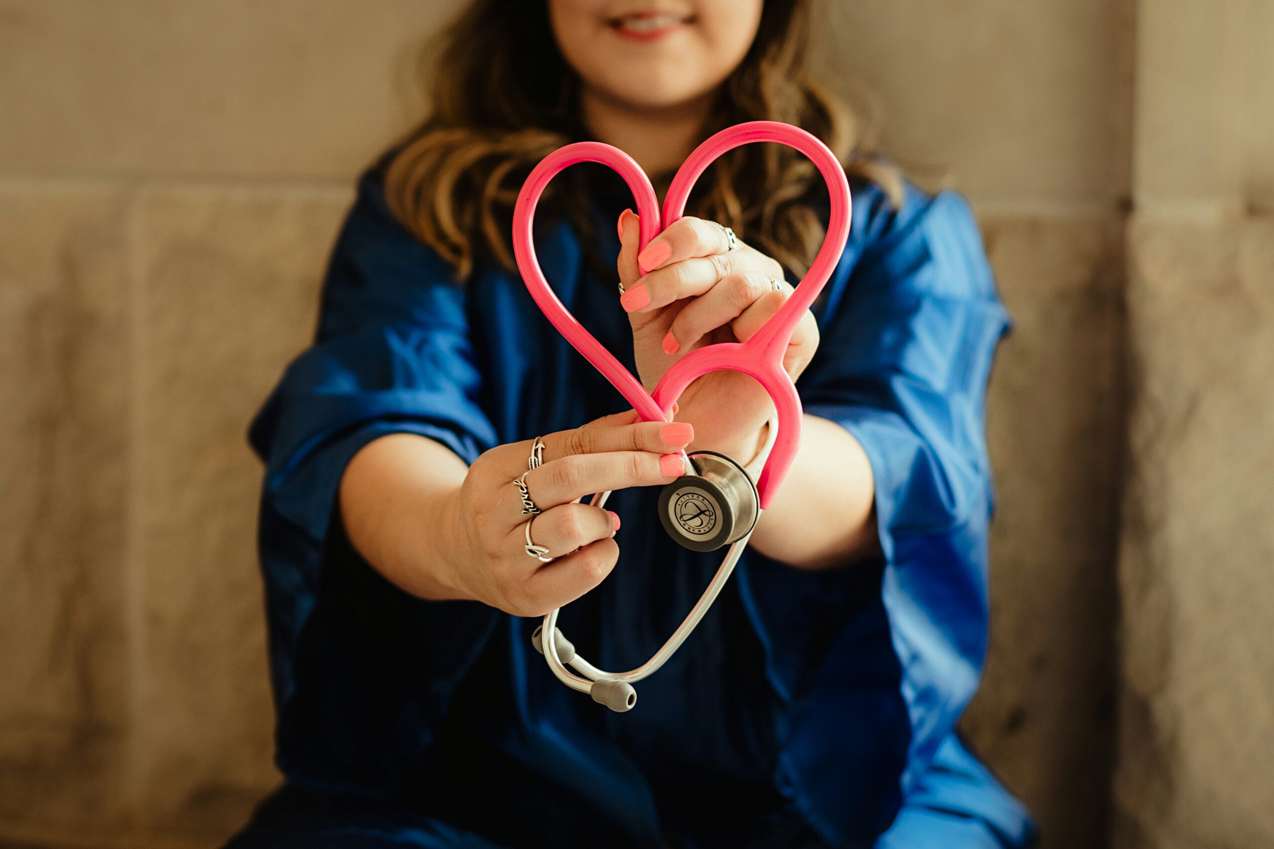 A woman holds a stethoscope shaped like a heart. 