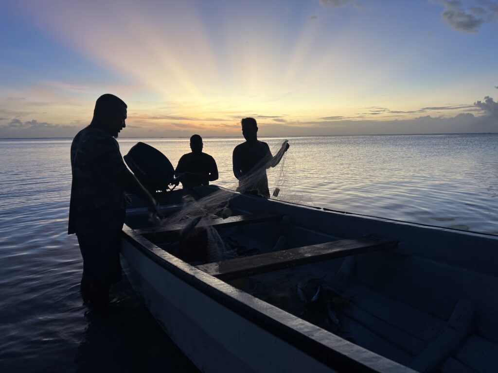 Fishermen pull a net into a small boat at sunset