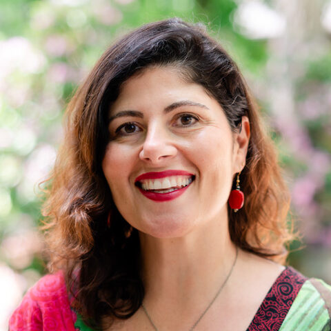 Desiree LaBeaud poses for a headshot in a colorful top against a natural backdrip