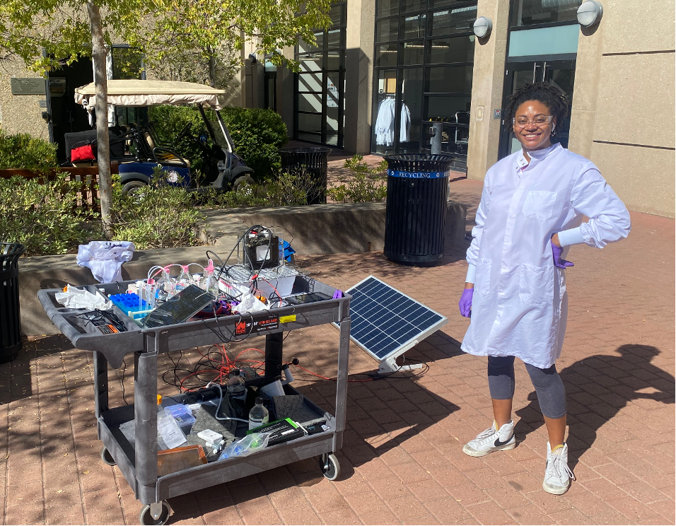 Mechanical Engineering PhD student and Knight-Hennessy Scholar Orisa Coombs with a solar-electrochemical stripping setup for outdoor experiments. The solar panel is cooled by water that is used to enhance nitrogen recovery from urine (synthetic urine in this experiment, real urine in several others).
