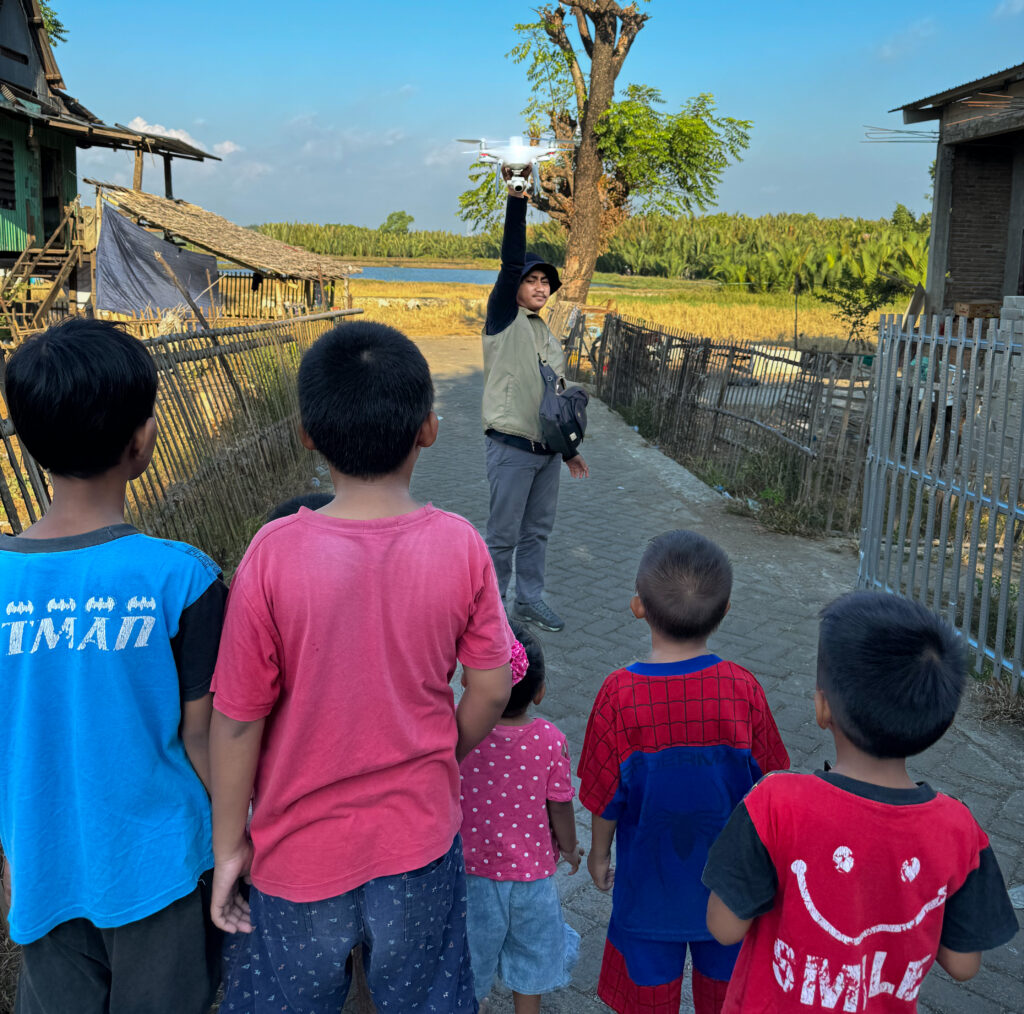 A local drone pilot (Muh. Yusuf Fadhel Marwiji) in  Makassar, Indonesia prepares to launch a drone to search for tires as curious children watch. Photo by Morgan Tarpennng.