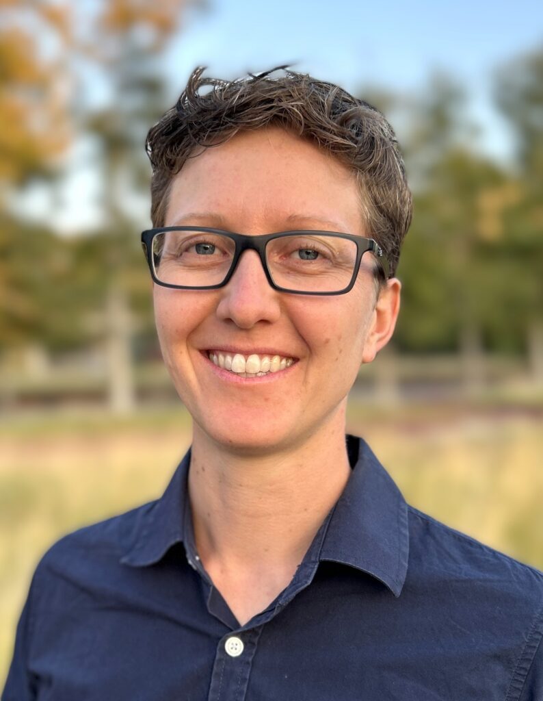 Nathalie smiles in an outdoor setting in a button up shirt