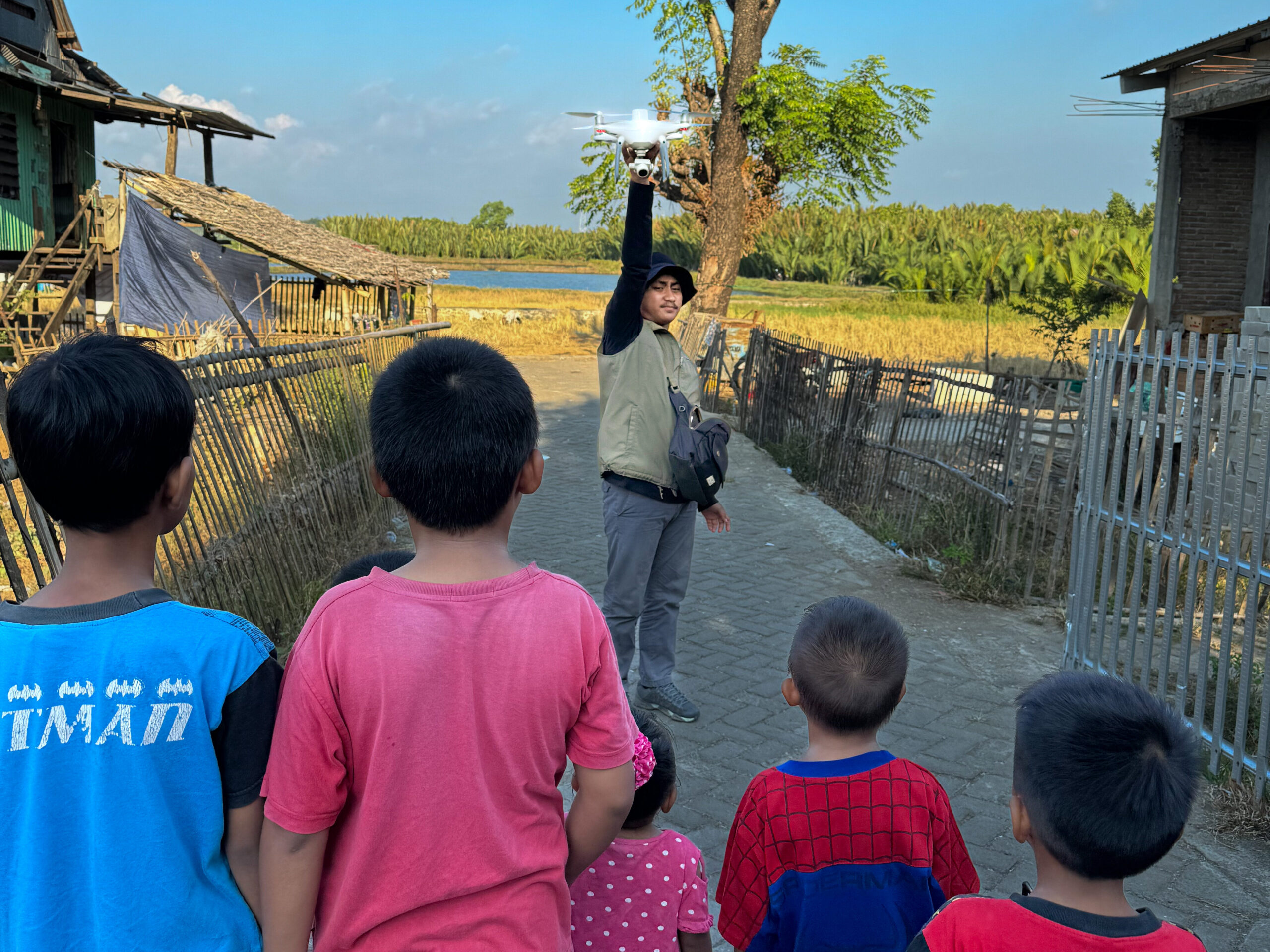 A local drone pilot (Muh. Yusuf Fadhel Marwiji) in Makassar, Indonesia prepares to launch a drone to search for tires as curious children watch. Photo by Morgan Tarpennng.